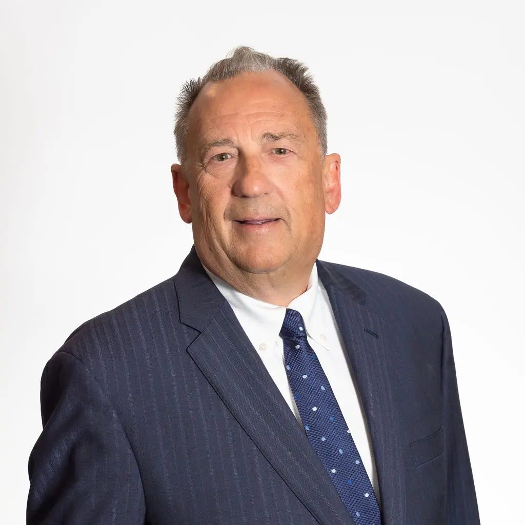 A man in a suit and tie standing up against a white wall.