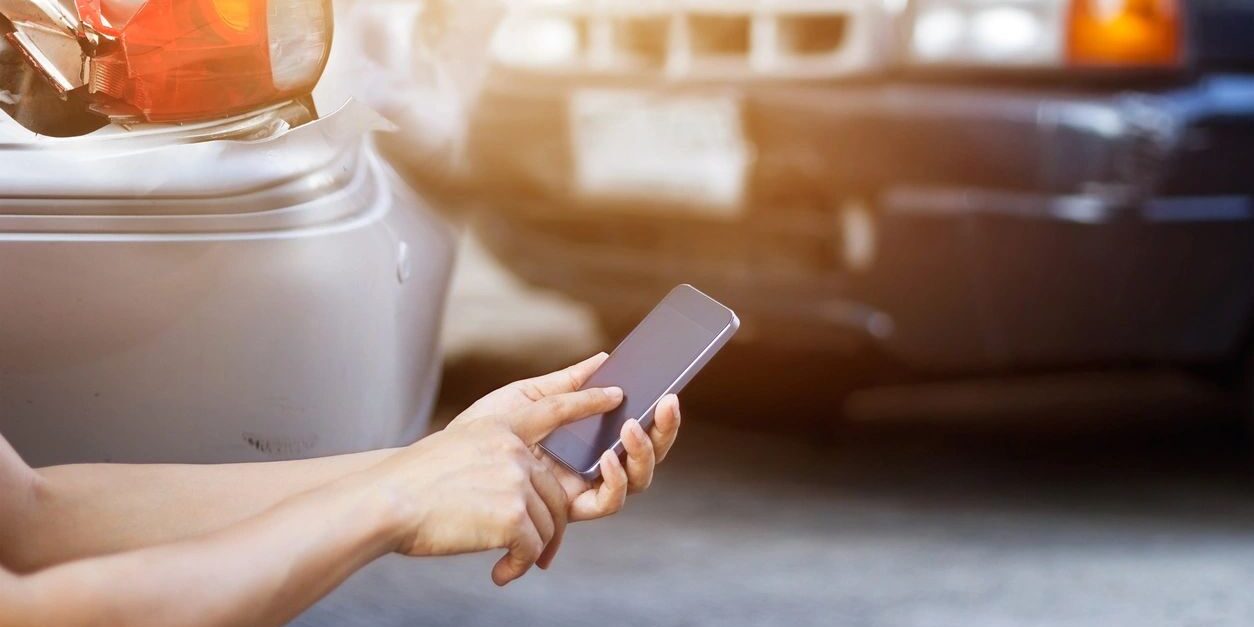 A person holding their cell phone in front of a car.